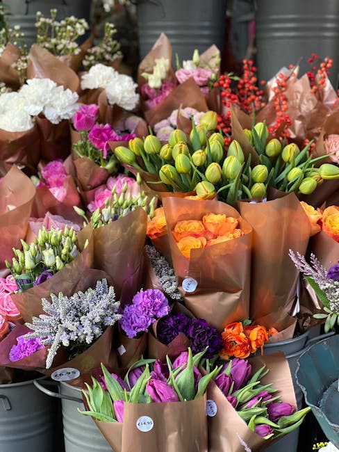 An array of fresh flower bouquets arranged in metal containers at a flower shop, showcasing a variety of blooms including white hydrangeas, pink and purple carnations, orange roses, purple statice, an