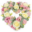 A lush, heart-shaped floral wreath fills the frame, its pastel colours glowing softly against a plain white background, reminiscent of the calm, elegant terraces of Notting Hill. The heart is fully covered with flowers, creating a rich, seamless surface of petals. Creamy ivory and pale lemon roses form the central rhythm of the design, their swirling centres and rounded heads conveying a sense of grace and enduring affection. Between them, layers of pale pink carnations introduce a soft, ruffled texture, their many petals catching the light in gentle, feathery ripples. Deeper rose-pink and mauve lisianthus blooms are scattered throughout, their more open, fluted forms lending depth and a touch of contemporary refinement. Small yellow-green buds poke through the arrangement, hinting at freshness and new beginnings even in a time of farewell. Cool eucalyptus foliage in a muted silvery-green tone winds gracefully around and within the heart, its rounded leaves offering both structure and a soothing, herbal character. The overall design is balanced and symmetrical, with the heart shape clearly defined and every stem placed with intention. It feels like a quiet embrace of flowers, ideal for funeral services, remembrance gatherings, or anniversary memorials held in churches and crematoriums around Notting Hill and nearby Bayswater. The mood is gentle, respectful, and deeply compassionate, providing a visual expression of sympathy, love, and treasured memories when words alone are not enough.