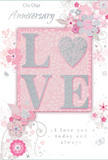 This anniversary card is designed in the same soft, romantic spirit as a pastel bouquet delivered on a calm evening in Notting Hill. Dominating the centre is the word LOVE, spelled in raised letters coated with a delicate mixture of blush-pink, pearlescent white, and fine silver glitter. The surface looks beautifully tactile, as though you could feel each shimmer under your fingertips the way you'd feel the layered petals of a garden rose. The letters rest against a smooth blush-pink background that glows gently, neither too bright nor too pale, giving the card a serene warmth. Flowing out from the central motif, clusters of stylised flowers and spiralling leaves create a soft, circular movement around the word. Their petals and foliage are drawn with slender, curling strokes, lightly shaded in pastel pinks, silvery greys, and soft whites that call to mind the muted romance of early spring bouquets seen along Westbourne Grove or tucked into quiet mews. Tiny details-fine filigree lines, subtle flourishes, and delicate heart-like shapes-thread between the blooms, suggesting both lightness and devotion. Some elements catch the light with a silvery sheen, hinting at foil accents that glimmer without overpowering the design. An elegant handwritten-style script conveys an anniversary greeting and words of enduring love, placed so it balances the floral motif without crowding it. Altogether, the card feels personal and heartfelt, a gentle celebration of shared years and cherished memories, as thoughtful as choosing fresh flowers for a familiar doorstep near Portobello Road.
